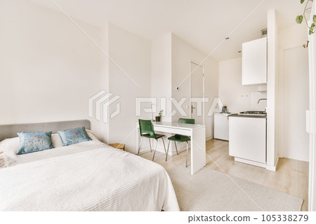 a bedroom with a bed, desk and small kitchen in the room next to the bed is a white refrigerator a bedroom with a bed, desk and small kitchen in the room next to the bed is a white refrigerator 105338279