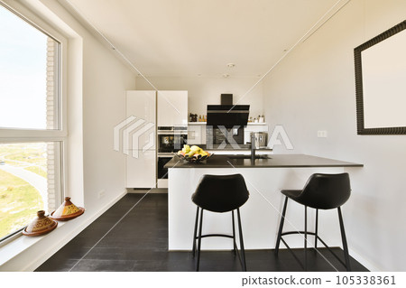 a kitchen with two stools in front of the counter and window looking out onto the street from the living room 105338361
