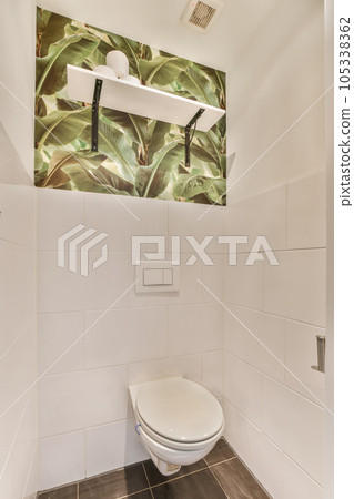 a toilet in a bathroom with plants on the wall behind it and a mirror over the toilet door to the right 105338362