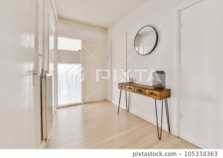 a hallway with white walls and hardwood flooring the room has a wooden console table on one side there is a large round mirror 105338363