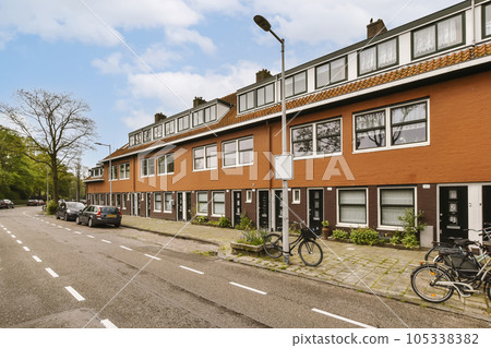 an urban street with parked cars and bicycles on the sidewalk in front of two buildings, one has a bicycle leaning against the wall 105338382