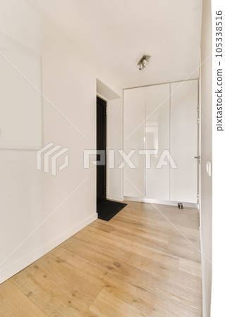an empty room with white walls and wood flooring on the right, there is a black door to the left 105338516