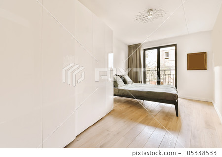 a bedroom with white walls and wood flooring, including a bed in the middle part of the room there is a large window 105338533
