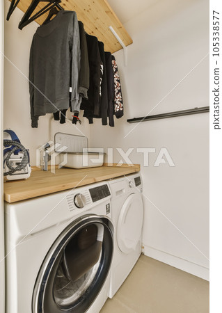 a laundry room with a washer and dryer on the wall, next to an ironing rack for clothes 105338577