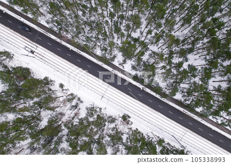 Aerial view on road in winter time, road surrounded with forest trees. Rural winter area. Top view landscape. shooting from drone. Snow covered road in winter forest 105338993