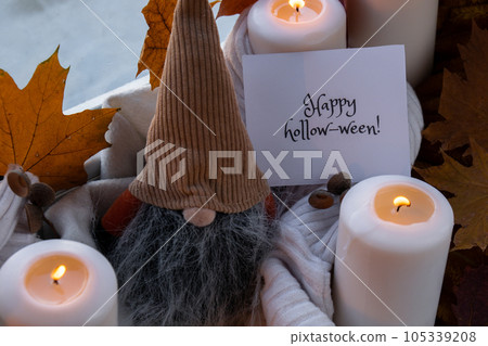 HAPPY HOLLOWEEN text greeting card concept Celebrating halloween autumn holidays at cozy home on the windowsill Hygge aesthetic atmosphere Autumn leaves gnome spices and candle on knitted white 105339208