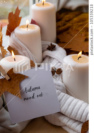 AUTUMN MOOD ON text greeting card concept Celebrating autumn holidays at cozy home on the windowsill Hygge aesthetic atmosphere Autumn leaves, spices and candle on knitted white sweater in warm yellow 105339218