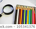 Colorful colored pencils and a magnifying glass on a white sheet of paper 105341376