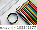 Colorful colored pencils, a magnifying glass and a ruler on a white sheet of paper 105341377