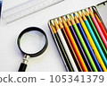 Colorful colored pencils, a magnifying glass and a ruler on a white sheet of paper 105341379