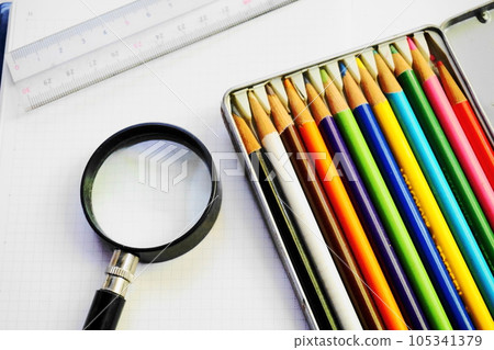 Colorful colored pencils, a magnifying glass and a ruler on a white sheet of paper Colorful colored pencils, a magnifying glass and a ruler on a white sheet of paper 105341379