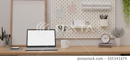 A laptop white screen mockup on a wooden table against the wall with white pegboard. 105341874