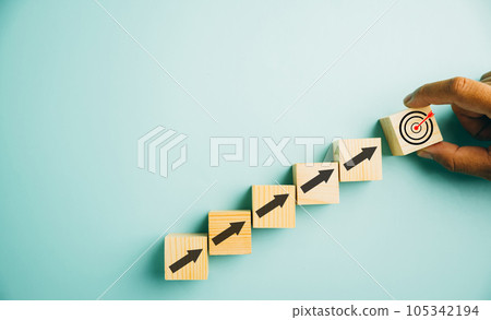 Wooden blocks with a prominent Target icon and rise up arrows. Bar graph chart steps illustrate business growth on a blue background. Represents profit, investment, and economic improvement concepts. 105342194