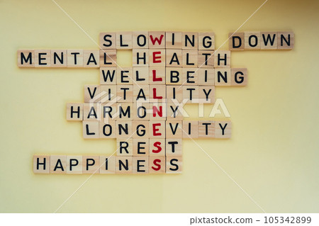 Top view of WELLNESS word on yellow background. Minimalism creative crossword puzzle concept. Message of text Slowing down mental health wellbeing vitality harmony longevity rest happiness 105342899