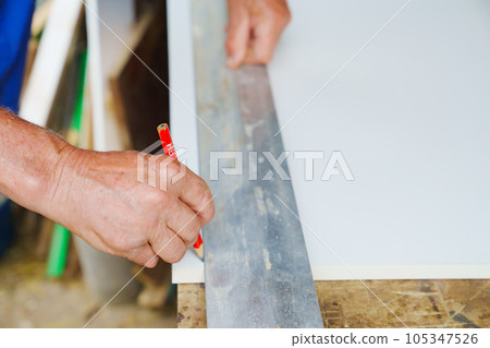 Men's hands take measurements and apply cut lines to chipboard. Men's hands take measurements and apply cut lines to chipboard. 105347526