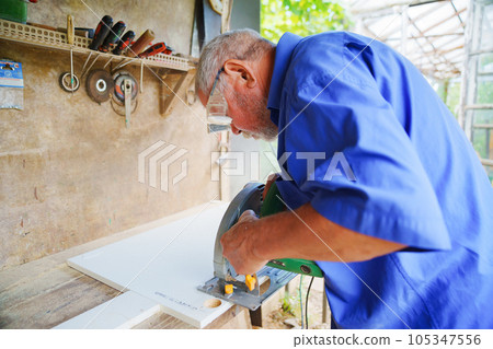 an elderly man in goggles with a circular saw an elderly man in goggles with a circular saw 105347556