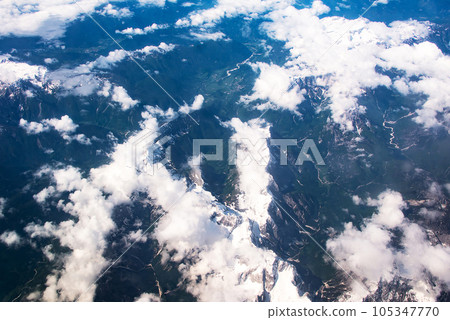 Beautiful window view of fluffy clouds and Alps mountains from passenger seat on airplane. Travel and air transportation 105347770