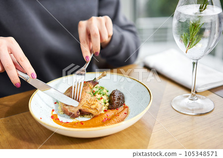 Lunch in a restaurant, a woman cuts delicious duck leg su-vide, with bulgur and onion marmalade. Barbecue restaurant menu, a series of photos of different meats 105348571
