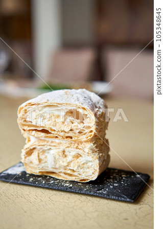 Breakfast in the cafe, morning coffee. Cappuccino and dessert Napoleon on the table. 105348645