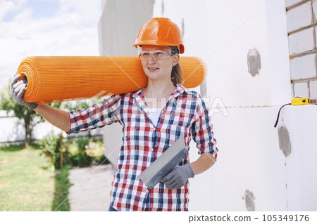 The woman with rolls of reinforcing fiberglass. Insulation of the house with polyfoam board on the facade 105349176