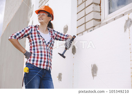 Insulation of the house with polyfoam. The worker is checking with the construction level the accuracy of the installation of polystyrene board on the facade. 105349210