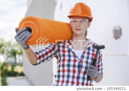 The woman with rolls of reinforcing fiberglass. Insulation of the house with polyfoam board on the facade 105349211