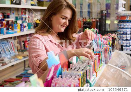 Pleasant female sales manager in school stationery store, arranging new pens on shelf for sale, working on merchandising 105349371