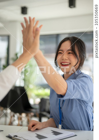 A cheerful Asian businesswoman gives high fives to a male colleague while working together. 105350669