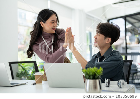 A happy Asian businesswoman gives high fives to a male colleague to celebrate a successful project 105350699