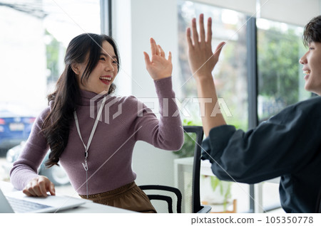 A cheerful Asian female worker gives high fives to a male colleague to cheer up 105350778