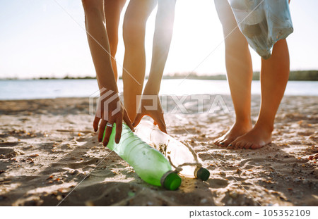 Three young girls pick up trash on the beach. Environmental pollution. Ecological problem. 105352109