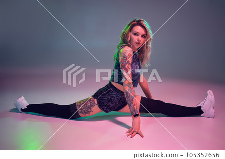 beautiful caucasian blonde girl in velour blue booty shorts and black stockings does stretching on pink background 105352656