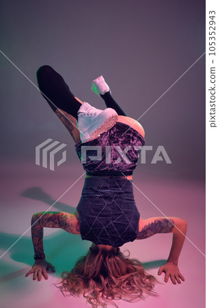young beautiful blonde gymnast girl in velour blue booty shorts and black stockings standing upside down on pink background 105352943
