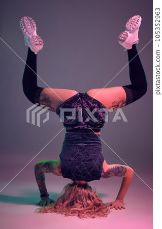 young beautiful blonde gymnast girl in velour blue booty shorts and black stockings standing upside down on pink background 105352963