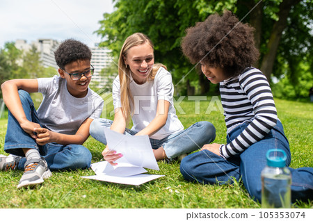 Blonde volunteer sitting on the grass and helping kids with tests Blonde volunteer sitting on the grass and helping kids with tests 105353074