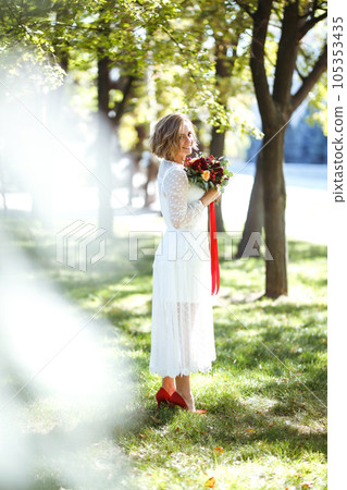 Beautiful bride with wedding bouquet in park. Elegant woman with professional make up and hair style 105353435
