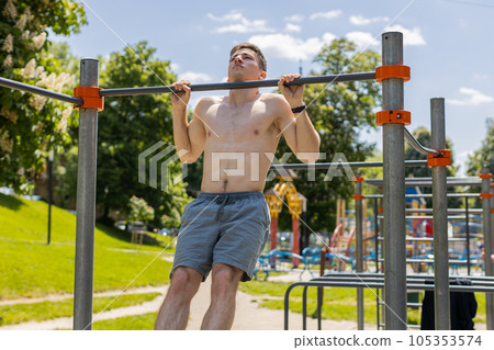 Athletic caucasian topless muscular man doing pull ups exercises on horizontal bar, pumping up back Athletic caucasian topless muscular man doing pull ups exercises on horizontal bar, pumping up back 105353574
