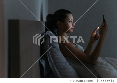 Young female addictively using her smartphone for chatiting late at night in her bed 105353615