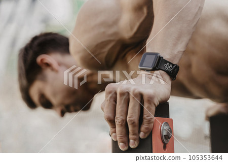 Closeup of athlete practicing calisthenics with smartwatch on his wrist. 105353644