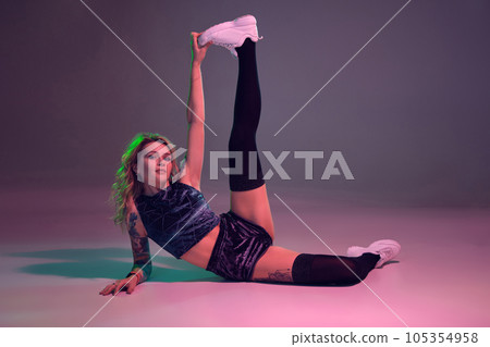 beautiful caucasian blonde girl in velour blue booty shorts and black stockings does stretching on pink background 105354958