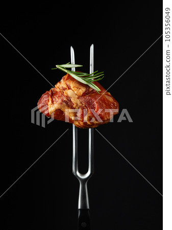 Smoked steak or ham with rosemary on a fork. Natural product from an organic farm. Menu for hotel on black background. 105356049