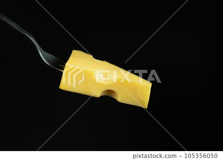 Sliced piece of milk cheese on a fork. Concept of street or fast food on black background. Copy space 105356050