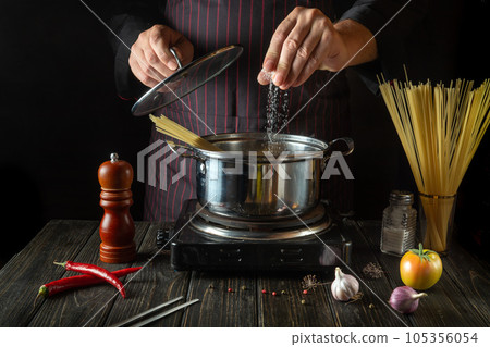 The chef salts organic pasta in a hot pot in the kitchen. Delicious hotel food recipe. Traditional Italian cuisine 105356054