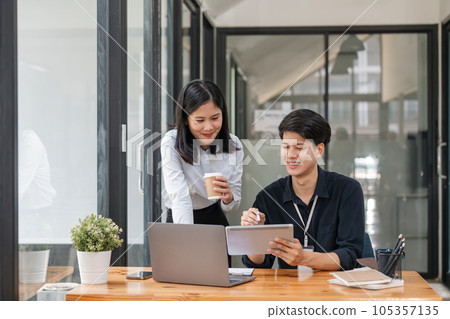 Two asian business worker looking at tablet discussing corporate strategy in teamwork, working on computer laptop in office at office Two asian business worker looking at tablet discussing corporate strategy in teamwork, working on computer laptop in office at office 105357135