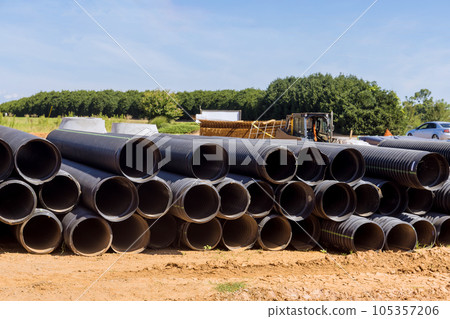 Large black plastic pipes for sewerage are stacked on the construction site, prepared for installation. 105357206