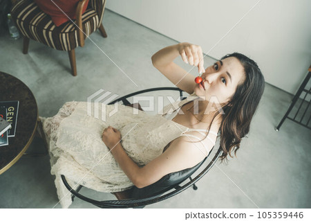 穿著白色連衣裙的年輕女子在室內拿著櫻桃 穿著白色連衣裙的年輕女子在室內拿著櫻桃 105359446