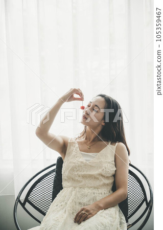 穿著白色連衣裙的年輕女子在室內拿著櫻桃 105359467