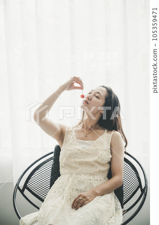 Young woman in white dress holding cherries indoors Young woman in white dress holding cherries indoors 105359471