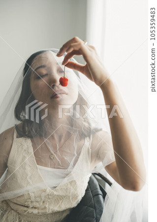 穿著白色連衣裙的年輕女子在室內拿著櫻桃 穿著白色連衣裙的年輕女子在室內拿著櫻桃 105359483
