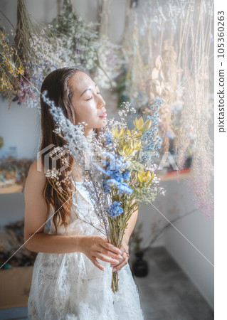 Beautiful woman in a white dress holding a bouquet of dried flowers 105360263
